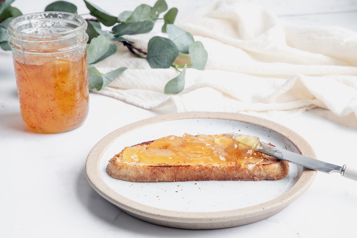 Horizontal beauty shot for Taste of Home Apple Jam spreading on toast while on a plate on top a marble surface.