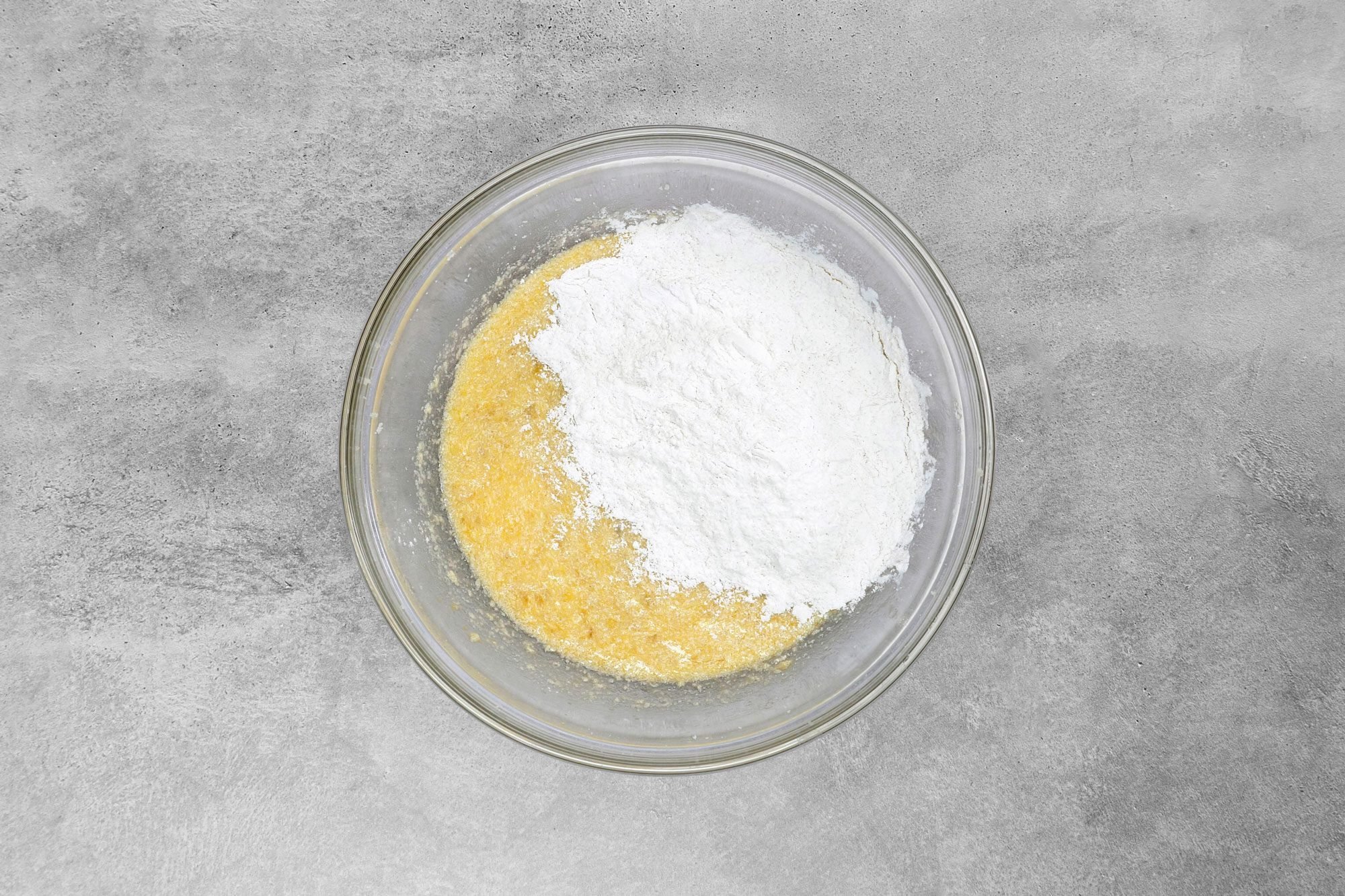 overhead shot; grey background; Combined the flour, baking powder, salt, baking soda and cinnamon in egg and banana mixture;