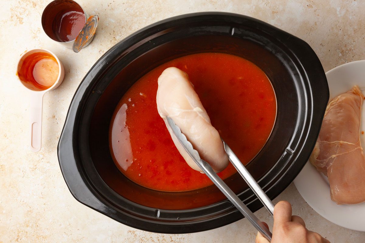 Step 1 of Taste of Home Buffalo Chicken Chili is to combine the navy beans, chicken broth, fire-roasted diced tomatoes, tomato sauce, buffalo sauce, onion powder and garlic powder in a slow-cooker. Then add the chicken and cover the slow-cooker. Cook the ingredients on low for five to six hours—or until the chicken is tender.