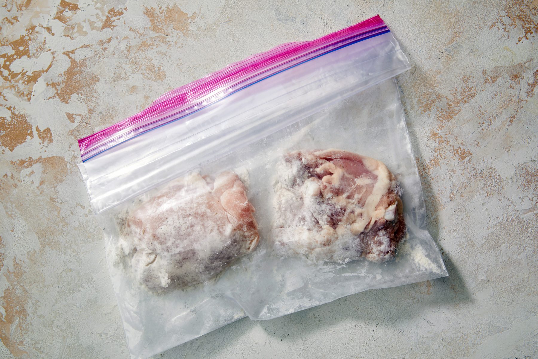 overhead shot; white textured background; Shaked to coat chicken thighs in plastic bag with flour