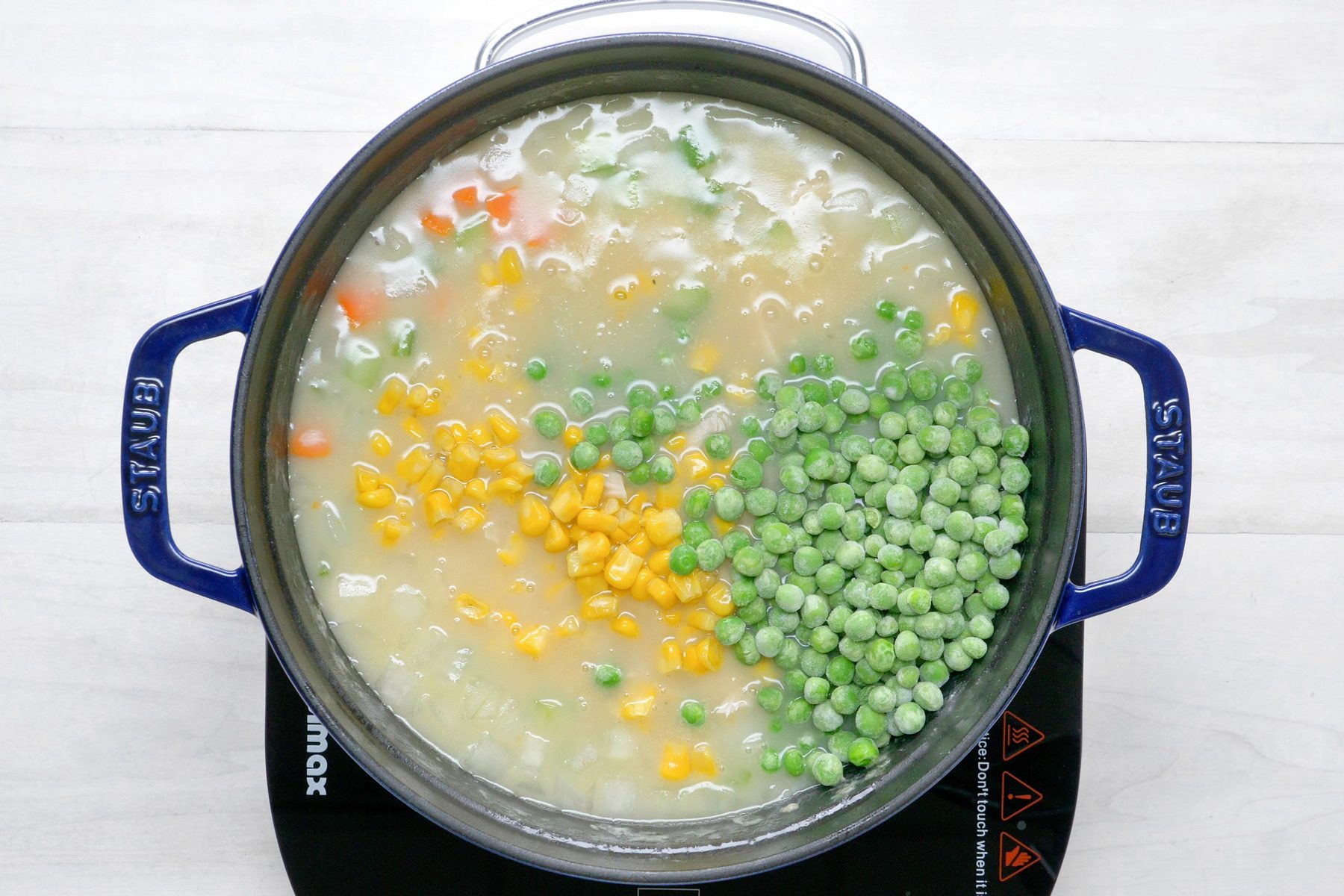 overhead shot; white wooden background; cooking vegetables with broth until tender in pan