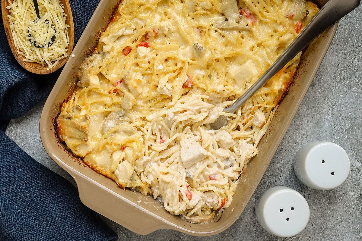 Creamy baked chicken tetrazzini being served, with Parmesan cheese on the side.