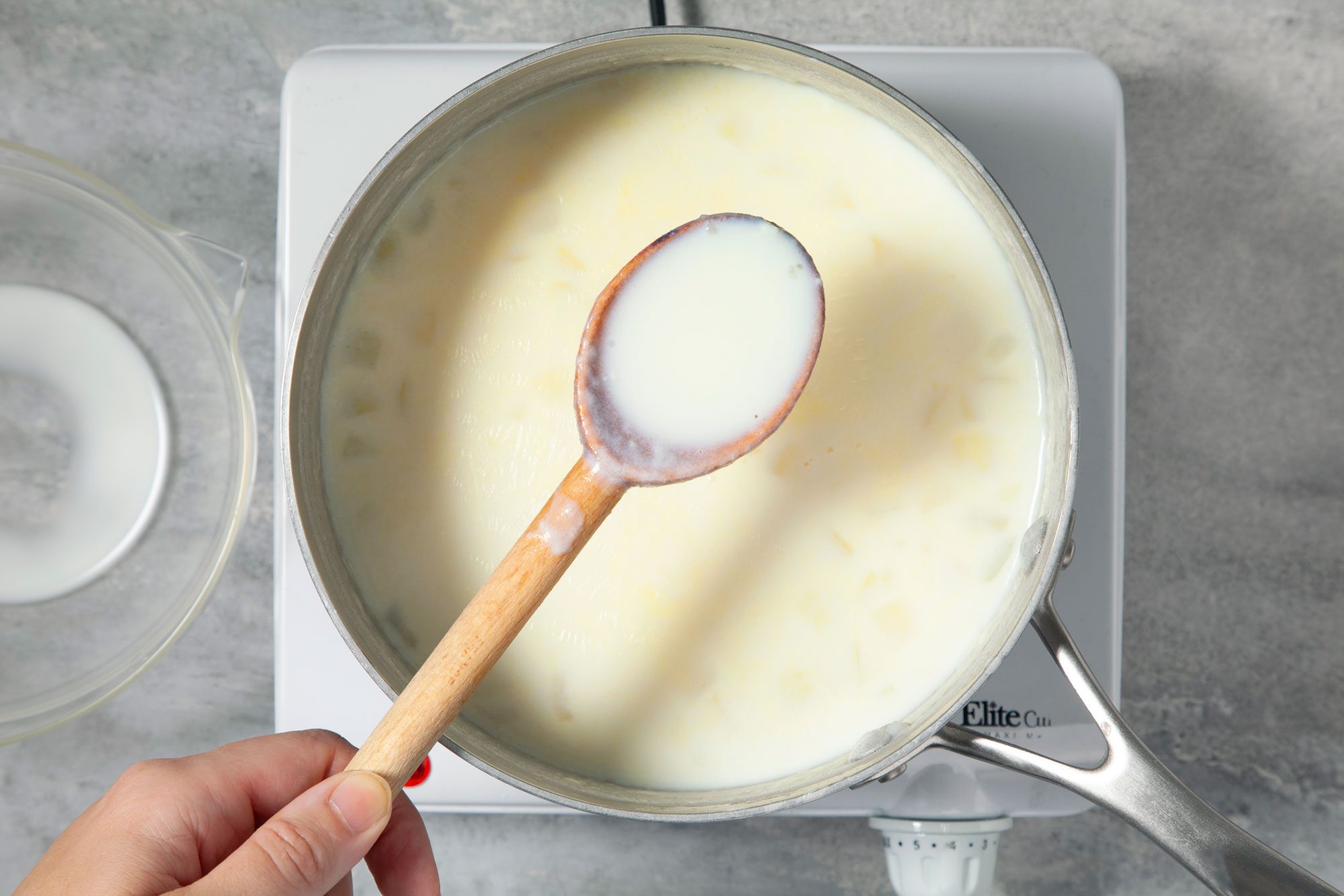A saucepan on an electric stovetop contains a creamy and white sauce