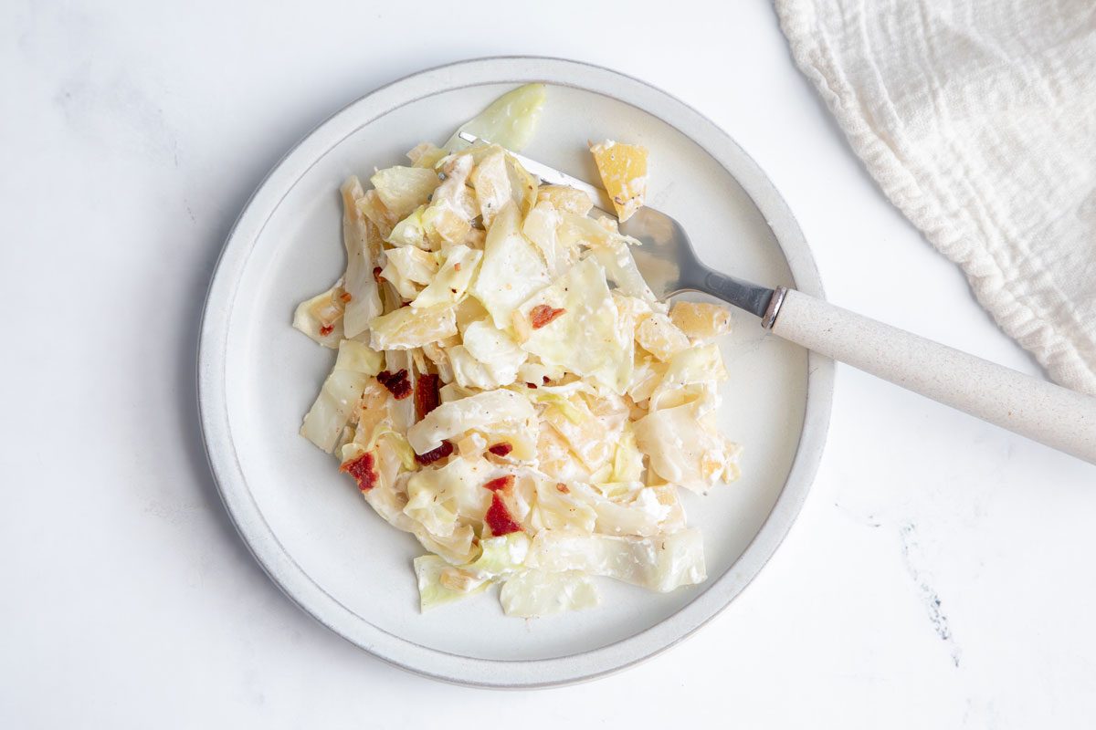 Overhead beauty shot for Taste of Home Creamed Cabbage topped with bacon on a marble surface.