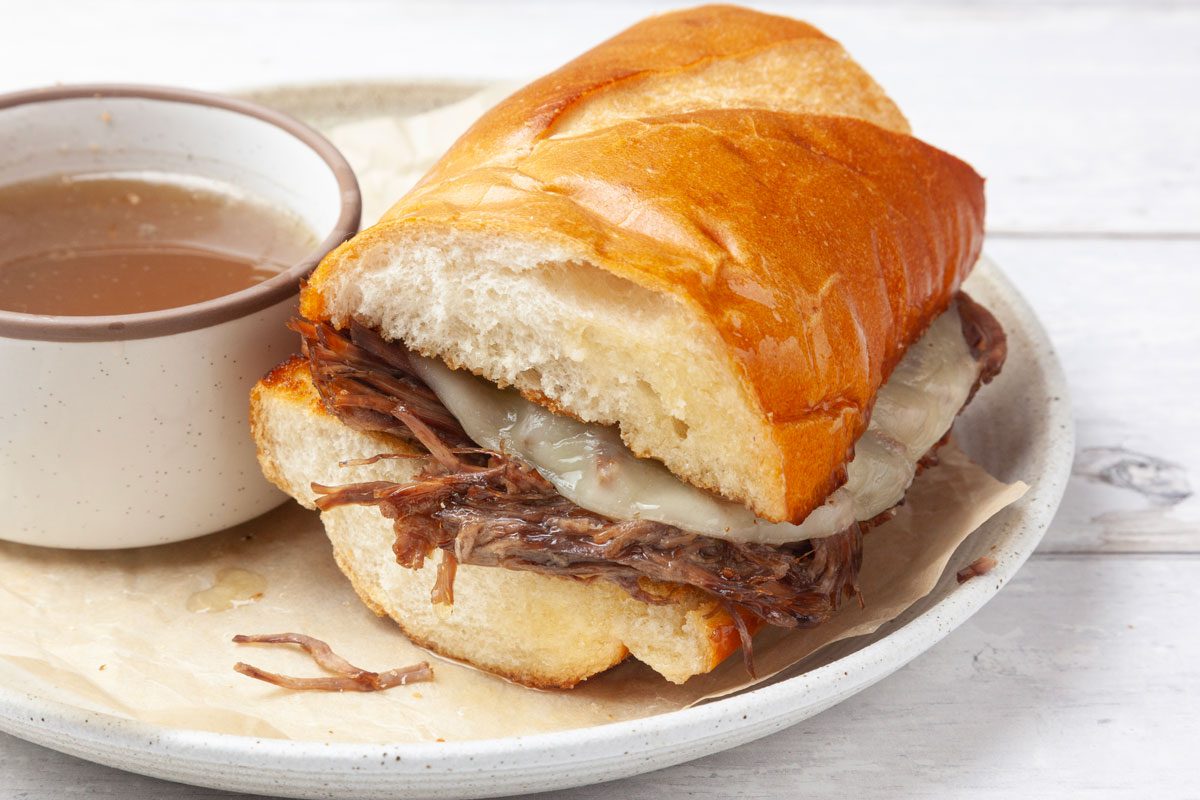 One servingsof Taste of Home Instant Pot French Dip with au jus on the side, provolone cheese, white wood surface