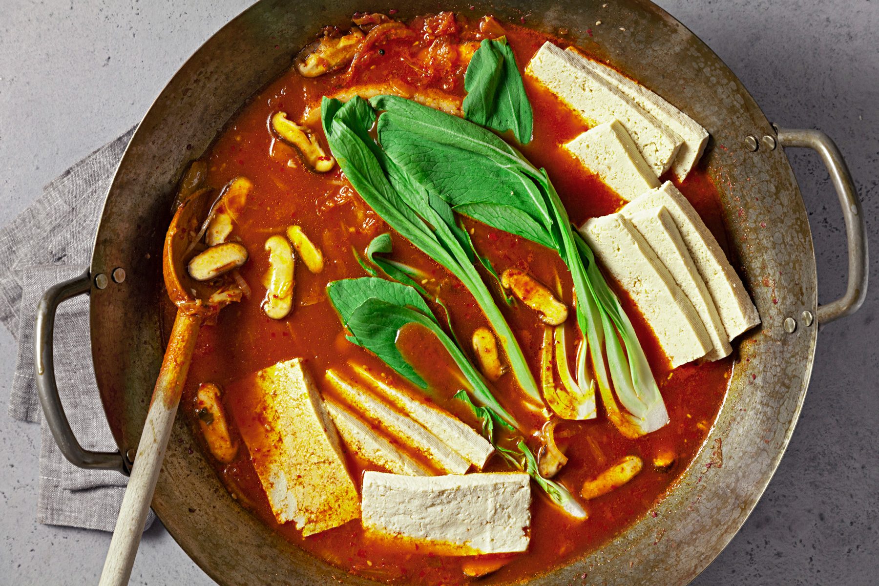 overhead shot; light grey background; Stired in tofu and bok choy in the wok