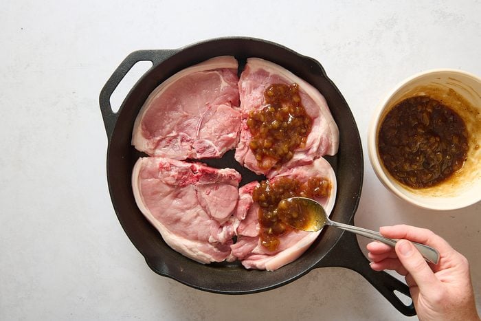 Spooning sauce over the pork chops in a large skillet