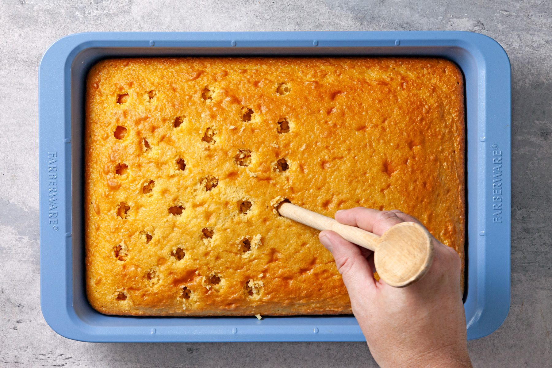 Overhead shot of cool completely in pan; using the handle of a wooden spoon; poke holes in cake; grey surface