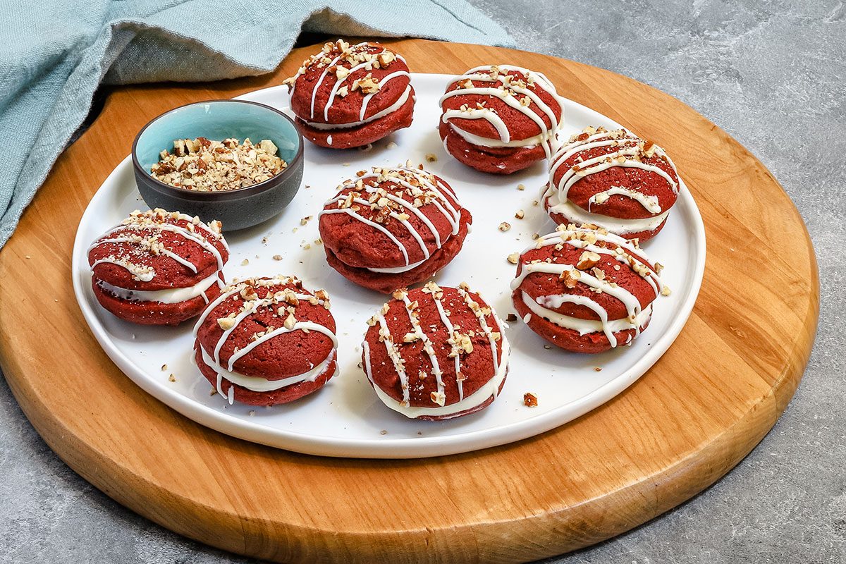 A plate of red velvet whoopie pies decorated with melted white chocolate and pecans.