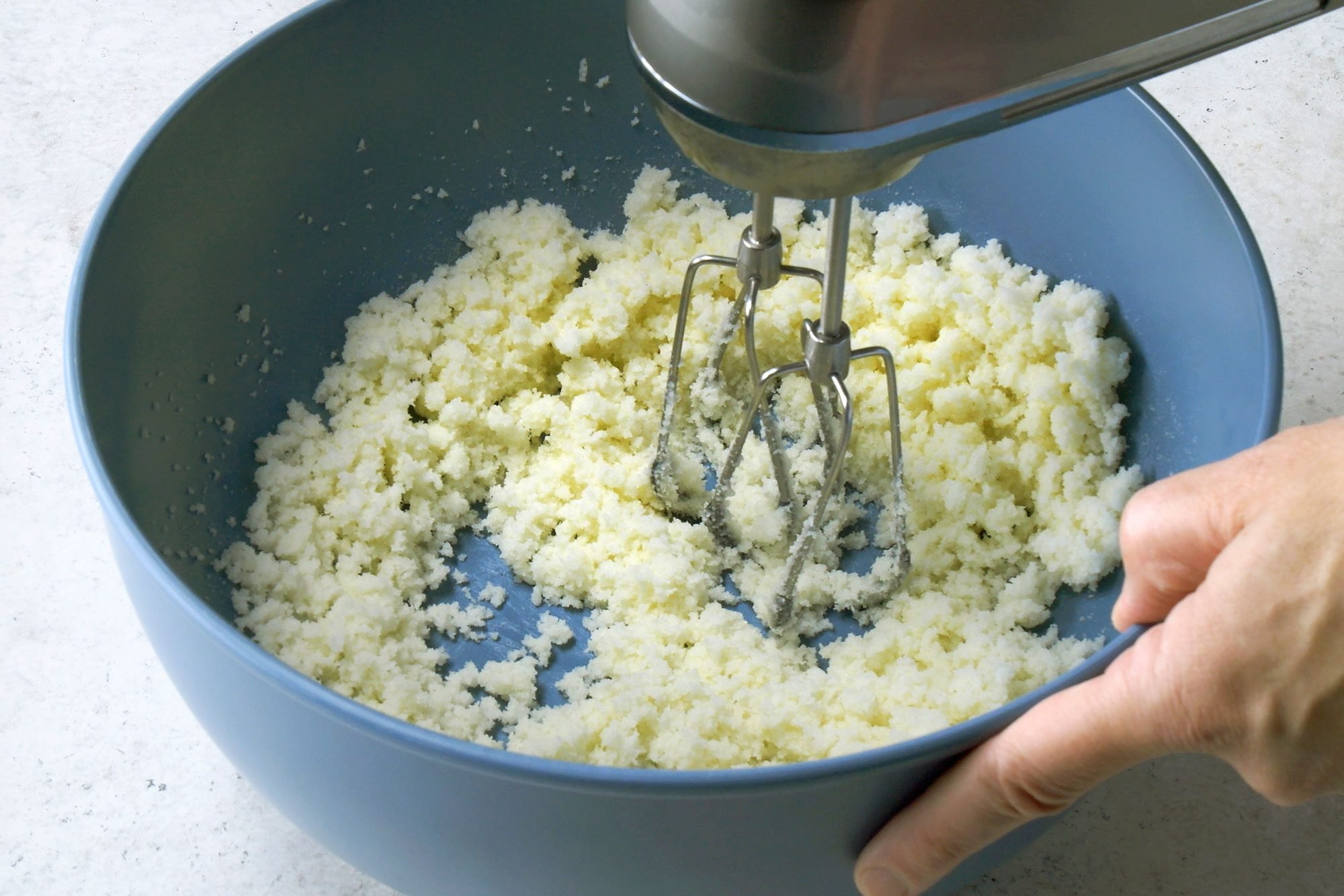 High angle view shot of a large bowl; beat cream butter and sugar until light and fluffy; blender; marble surface;