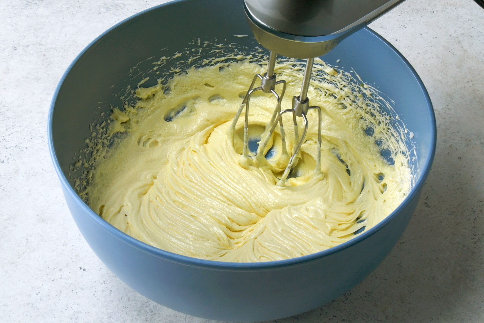 Close shot of the same bowl; add eggs; 1 at a time; beating well after each addition; beat in vanilla; blender; marble surface;