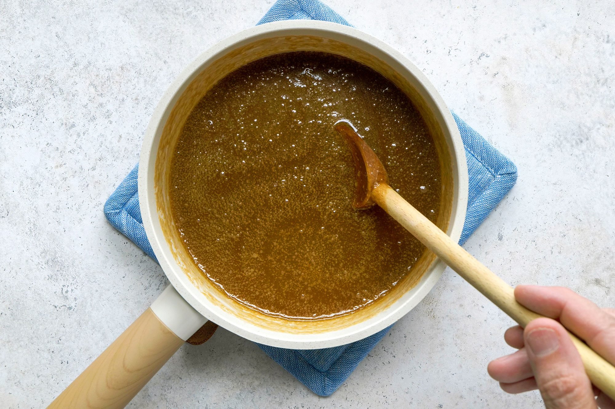 Overhead shot of remove from heat; stir in brandy and vanilla; serve sauce warm with warm cake; wooden spoon; marble surface;