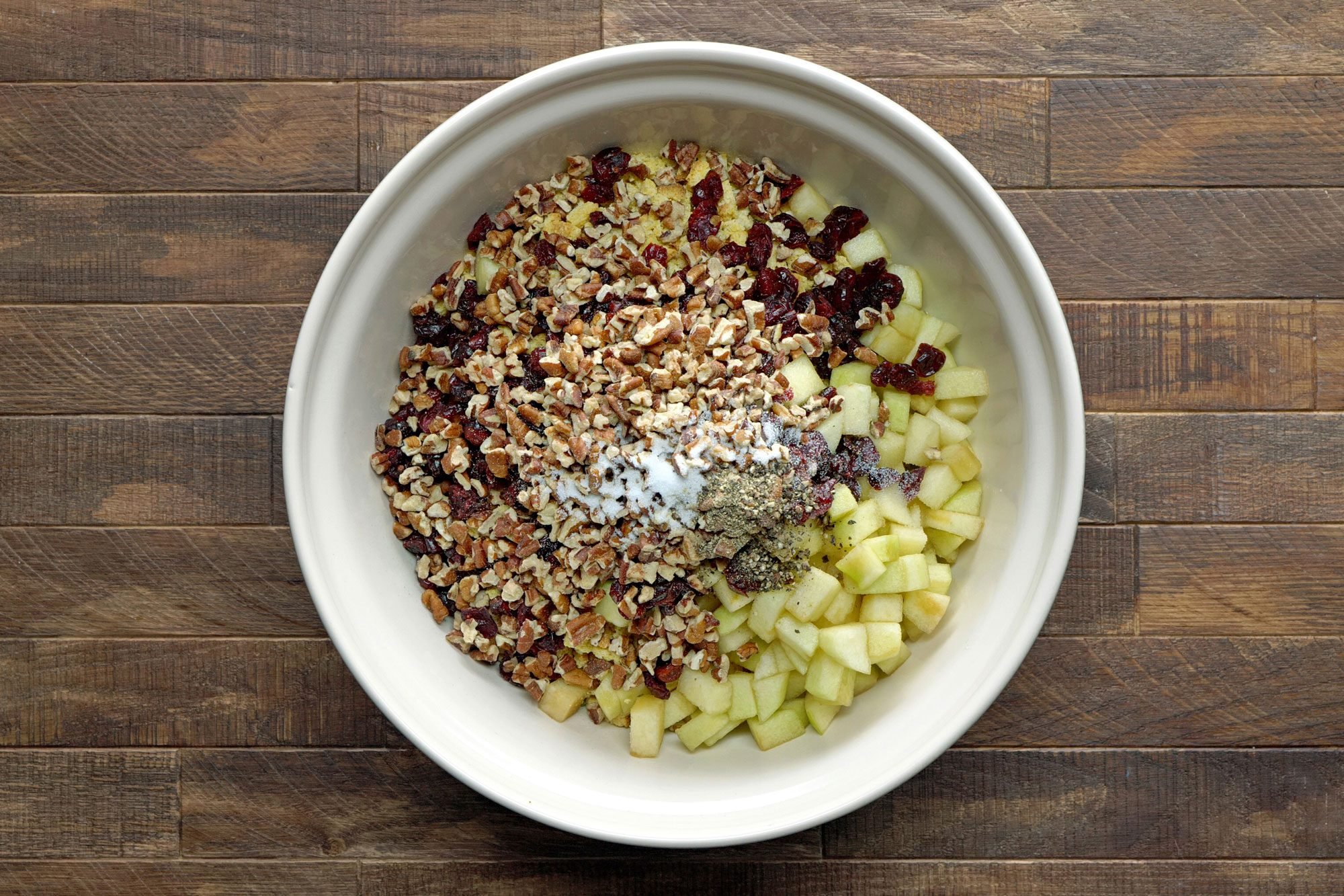 stuffing, apples, cranberries, pecans, salt and pepper in a bowl; Wooden Background;