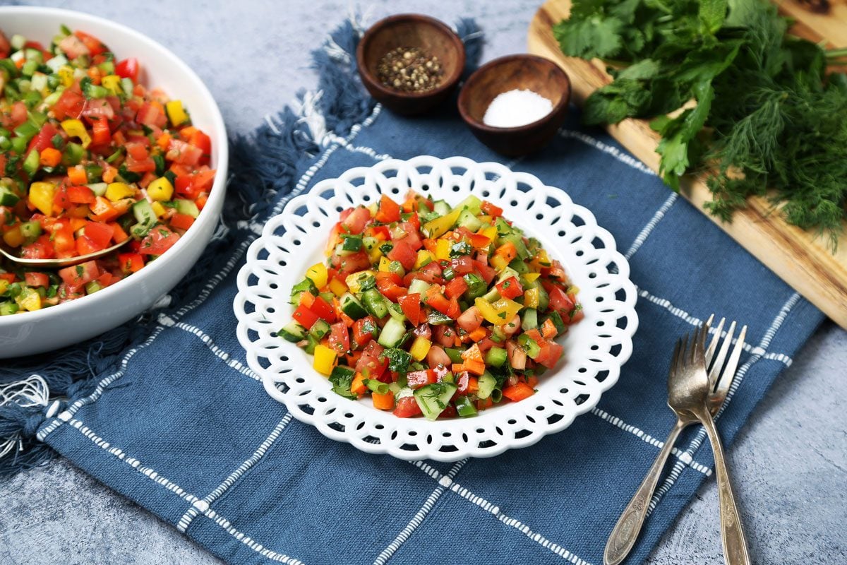 Close up of Taste of Home's Israeli Salad served on white plates on a blue linen and blue surface.