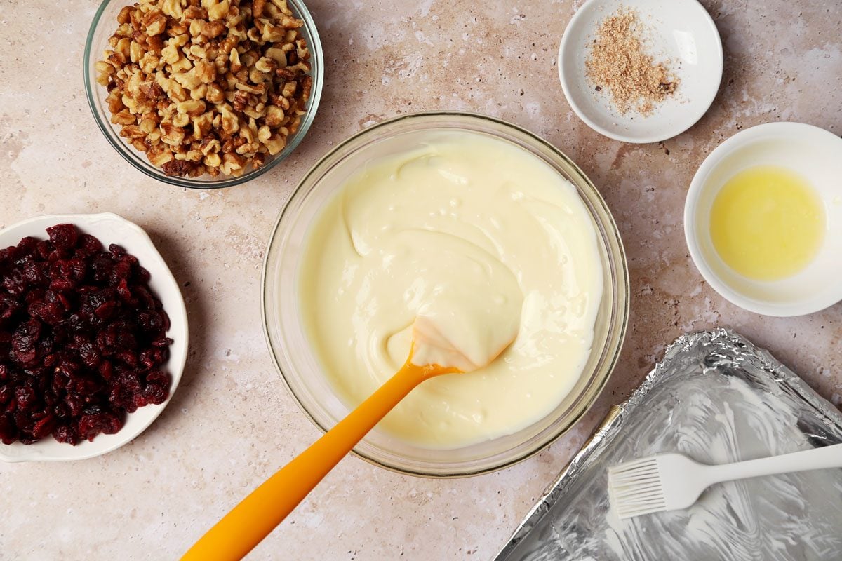 Process shot of the making of Taste of Home's White Chocolate Bark melting white chocolate in a mixing bowl on a beige surface.