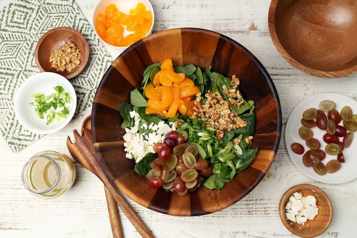 The process of how to make Taste of Home's Spinach Fruit Salad close up in a wooden salad bowl on a white wooden surface.