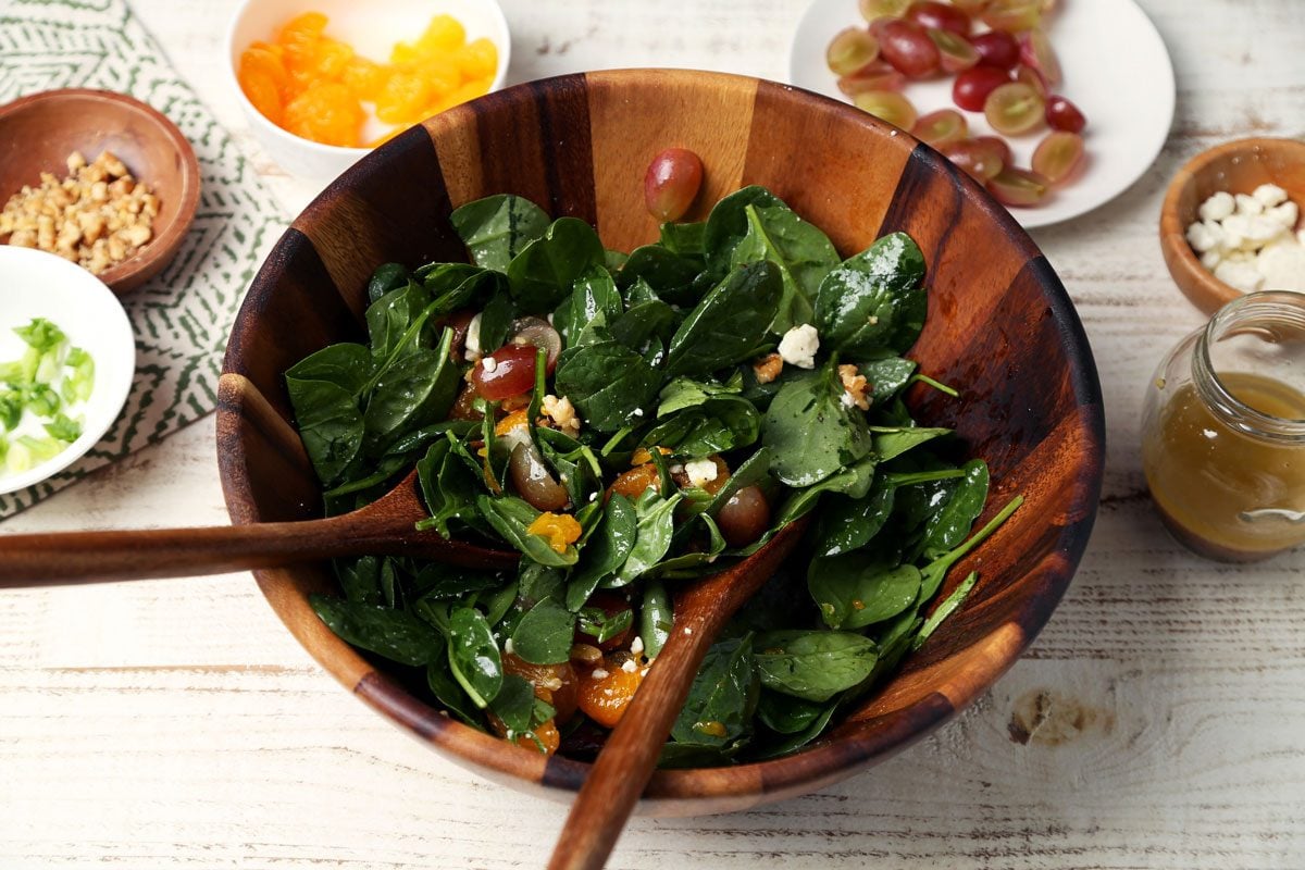 The process of how to make Taste of Home's Spinach Fruit Salad close up in a wooden salad bowl on a white wooden surface.