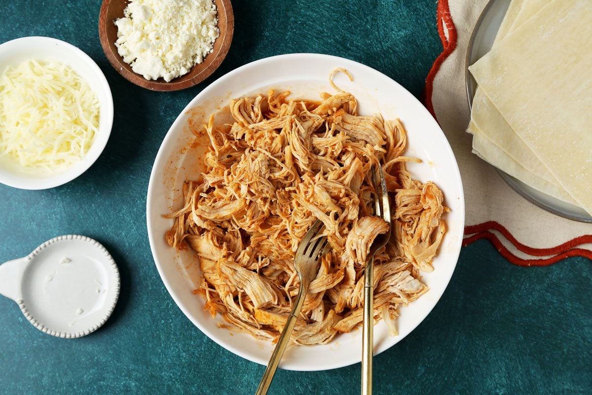 Process of making Taste of Home's Buffalo Chicken Egg Rolls. Buffalo chicken filling in a bowl on a green surface.