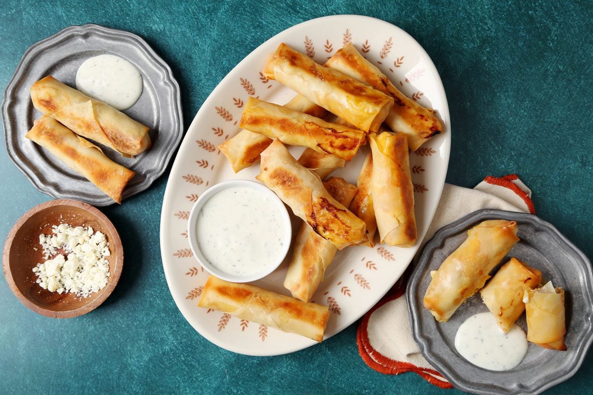 Close up of Taste of Home's Buffalo Chicken Egg Rolls on a serving dish on a green board.