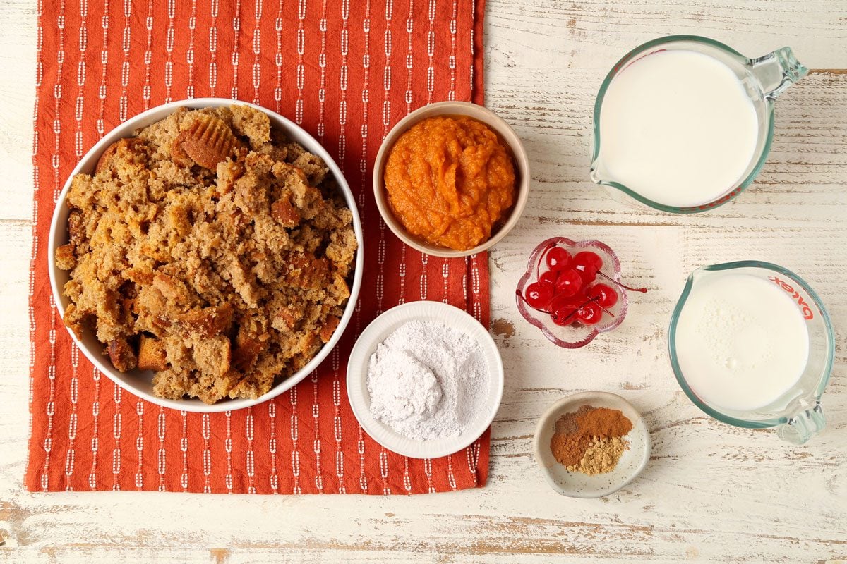 Ingredients for Taste of Home's Pumpkin Trifle laid out in small bowls on a white wooden surface with an orange towel.