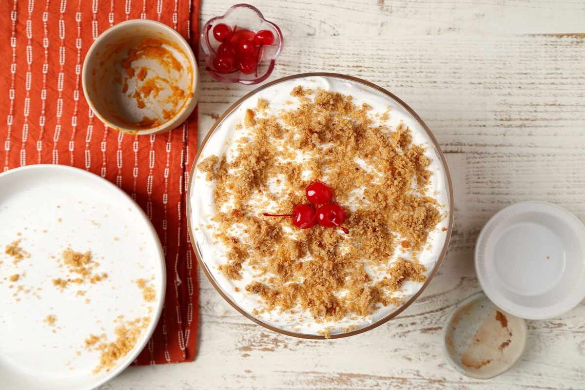 Process of making Taste of Home's Pumpkin Trifle layered in a glass serving bowl on a white wooden surface.