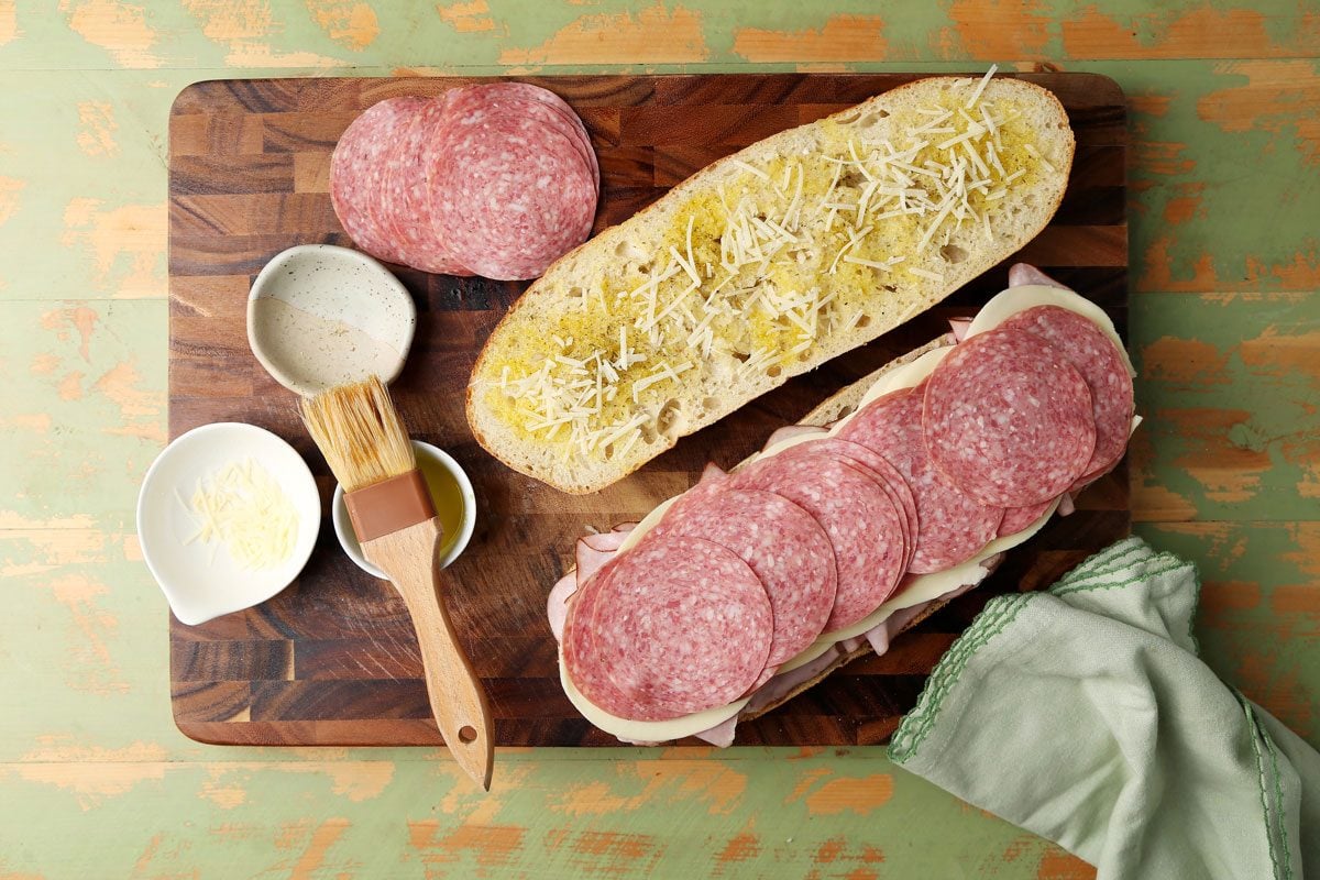 Close up of making Taste of Home's Italian Sub on a wooden board on a green surface.