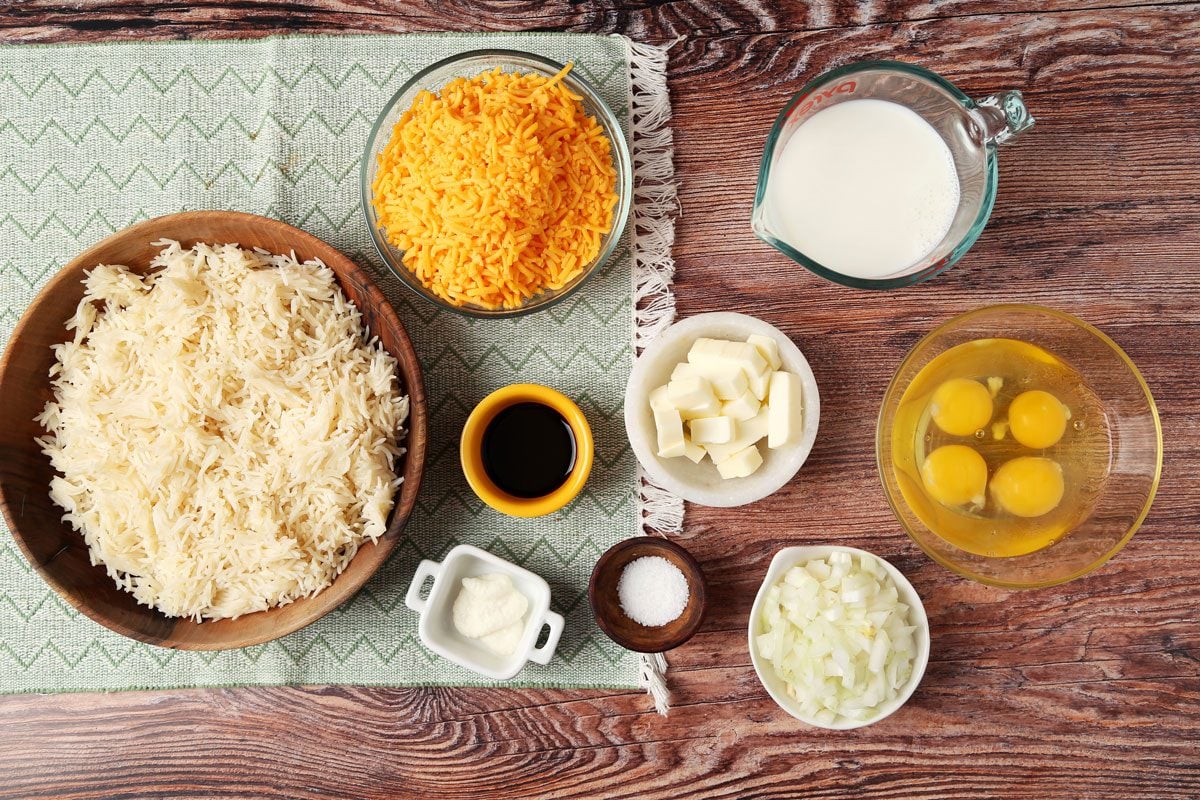 Ingredients for Taste of Home's Cheesy Rice Casserole laid out in small bowls on a brown wooden surface.
