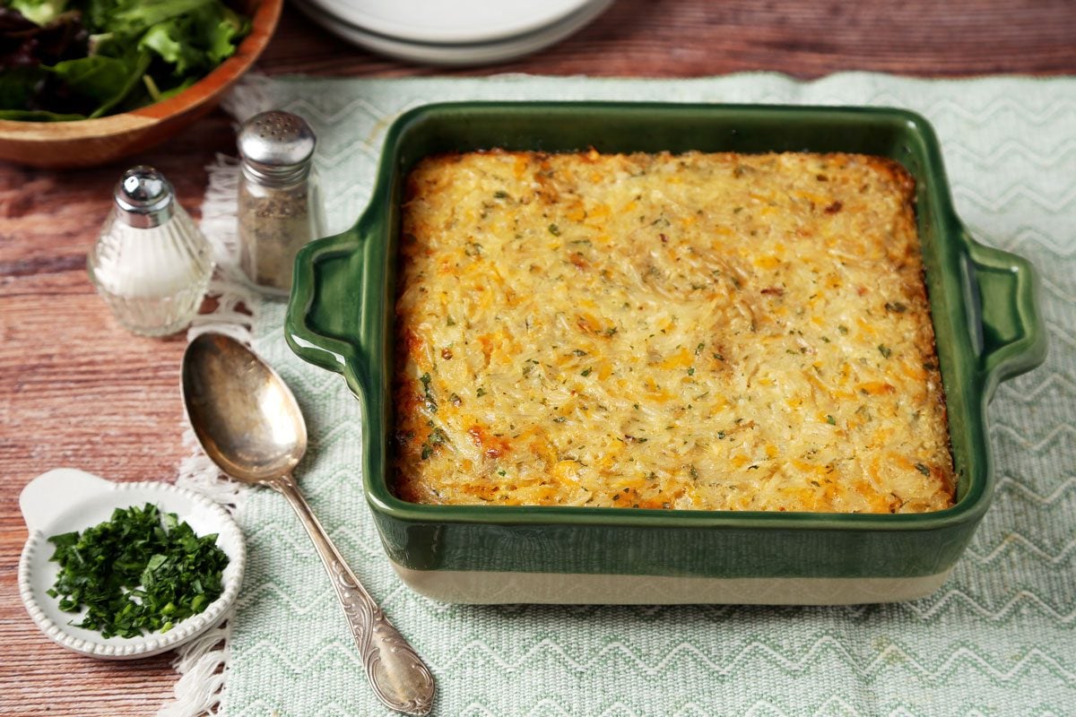 Close up of Taste of Home's Cheesy Rice Casserole baked in a green baking dish on a wooden surface.