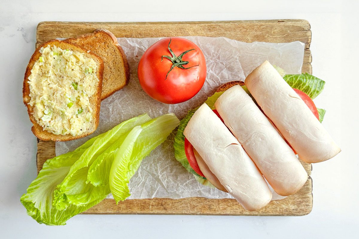 Taste of Home Turkey Avocado Sandwiches on a parchment lined wooden board with tomato and lettuce