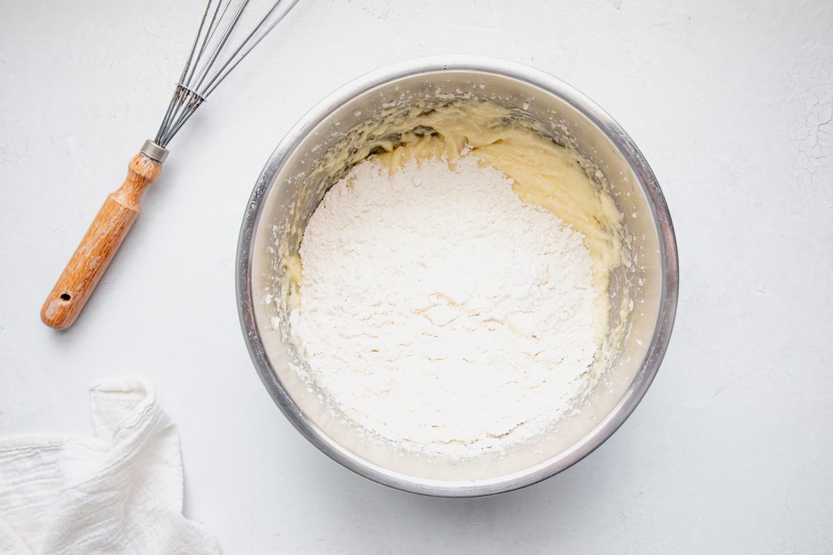 Batter for Taste of Home Waffle Cookies in a metal bowl not mixed with a whisk next linen on a marble surface.