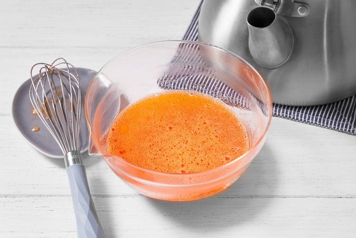 A bowl of orange liquid with bubbles in it