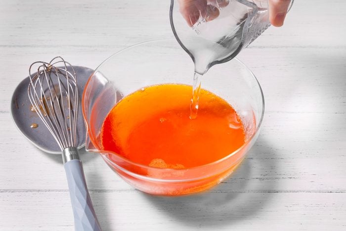 Water is being poured into a bowl of orange liquid