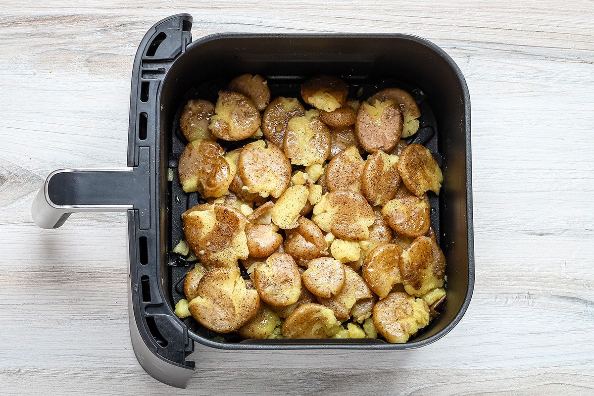 Smashed potatoes seasoned and ready to air-fry, in the air fryer basket.