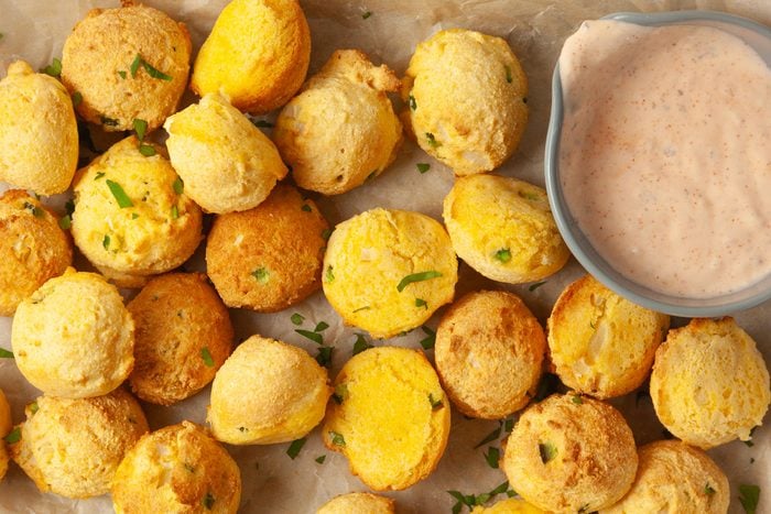 Close up of Taste of Home Air-Fryer Hush Puppies on a metal tray lined with parchment paper, remoulade dipping sauce