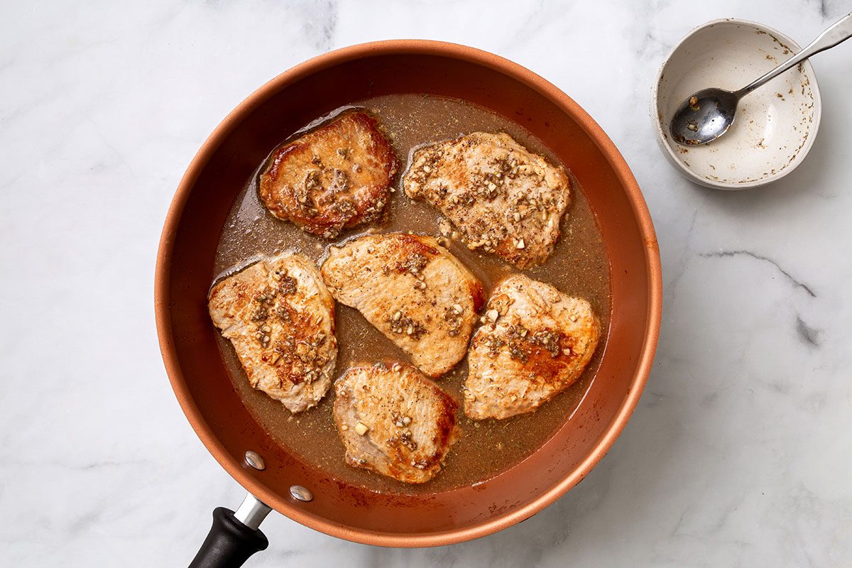 Apple cider sauce mixture poured on pork chops in large skillet for step two of Apple Cider Pork Chops recipes for Taste of Home