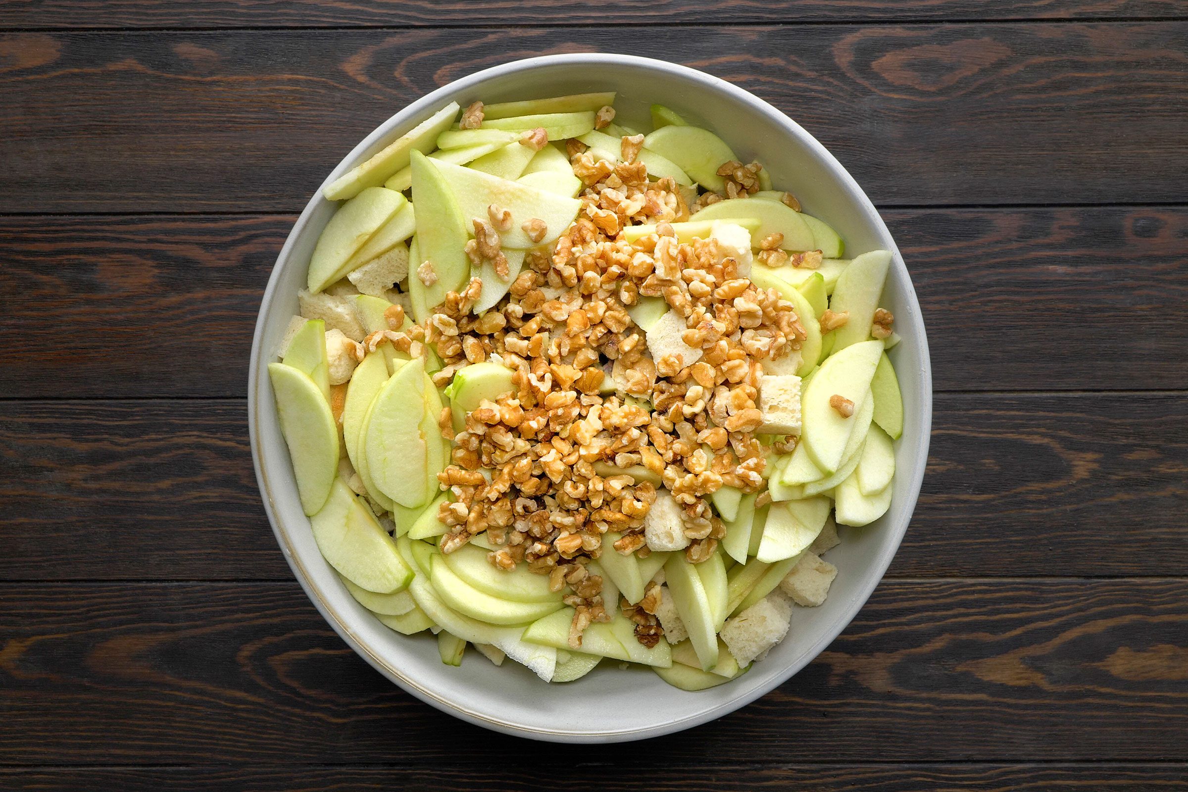 Apples, walnuts, herbs, spices, sausage and bread cubes in a bowl