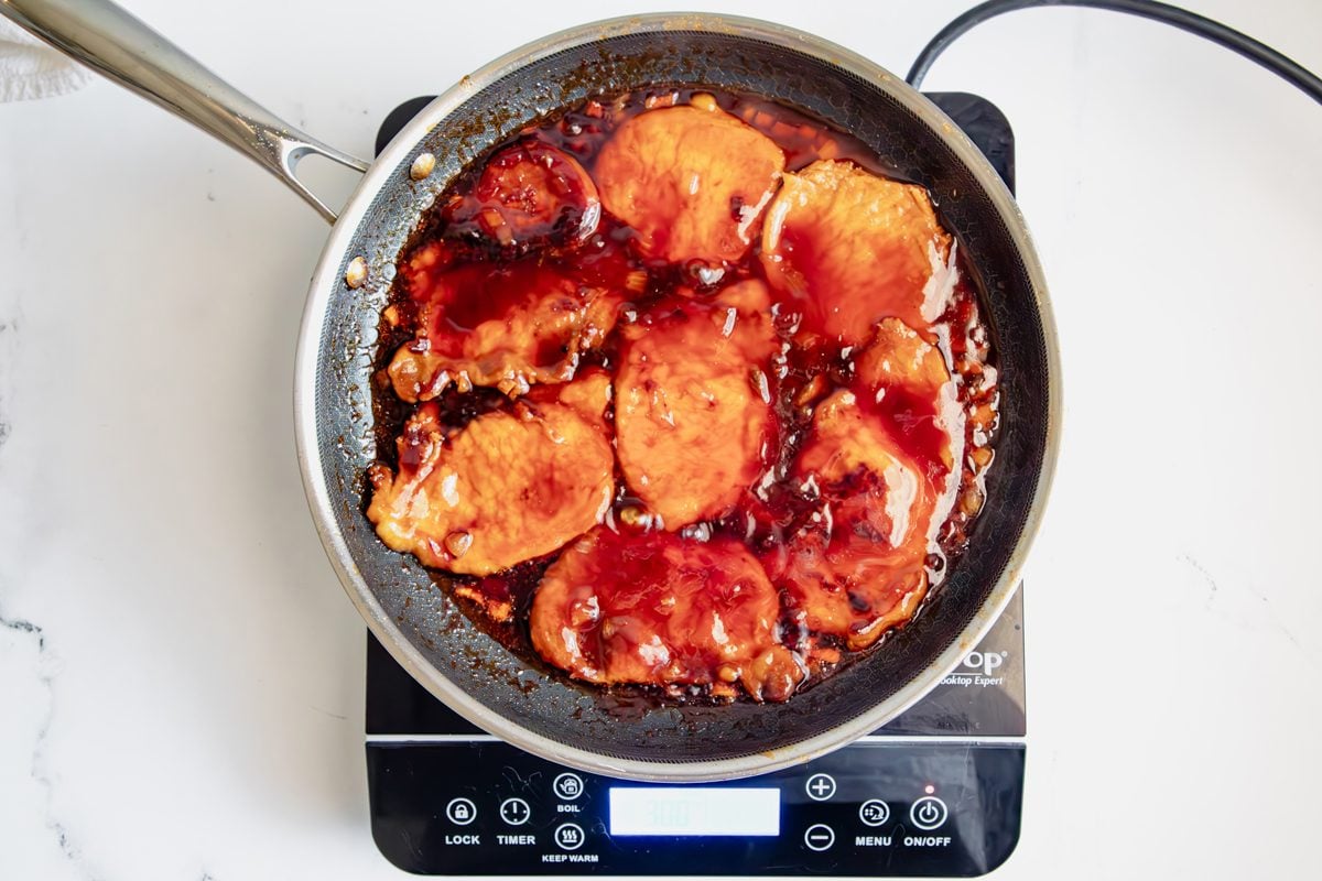 Overhead shot for Taste of Home BBQ Pork Chops cooking with BBQ sauce over an induction cooktop.