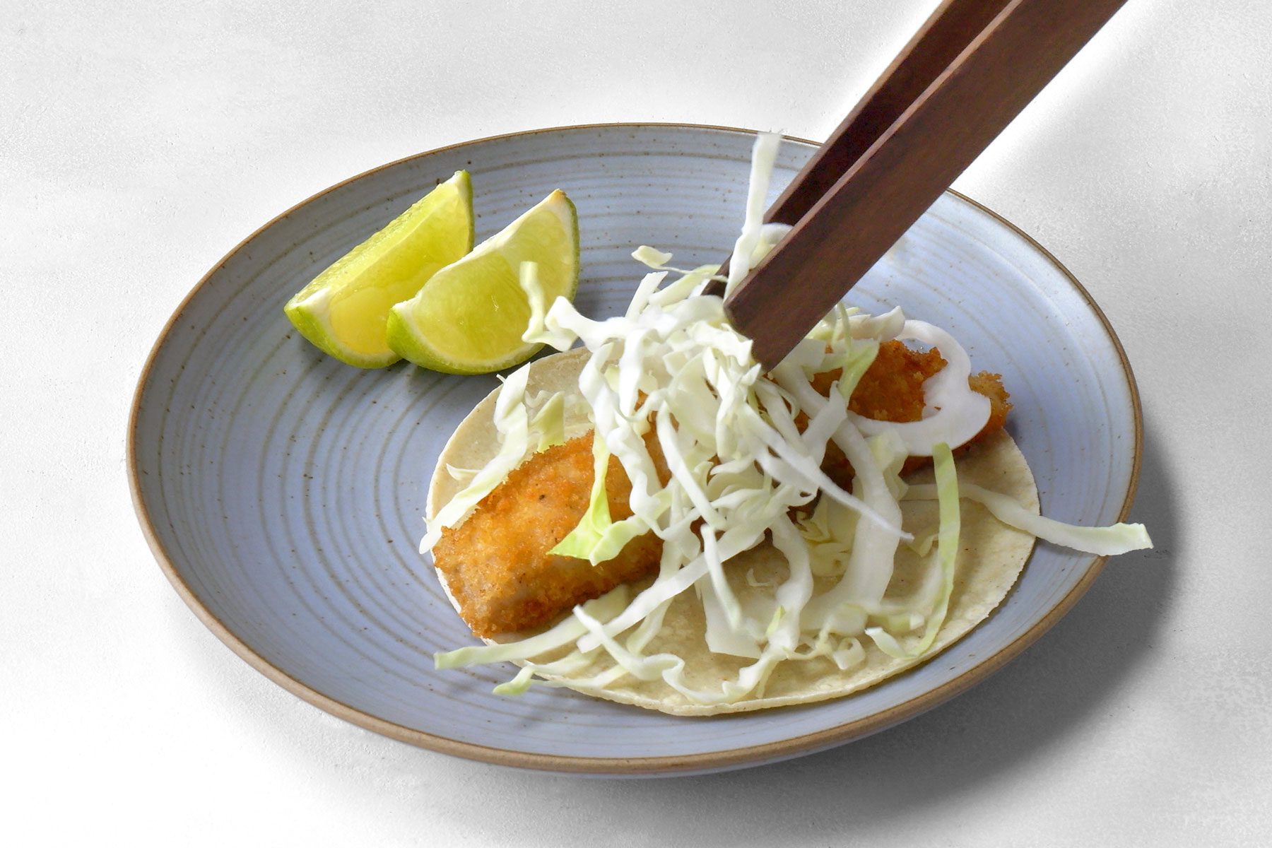 fried fish strip in a tortilla being topped with cabbage