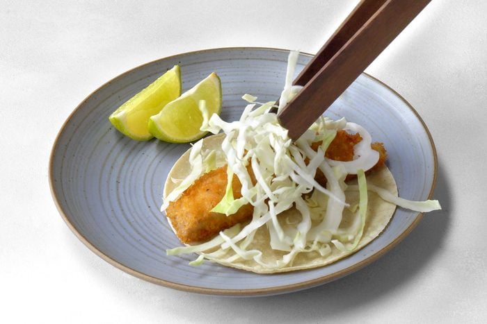 fried fish strip in a tortilla being topped with cabbage