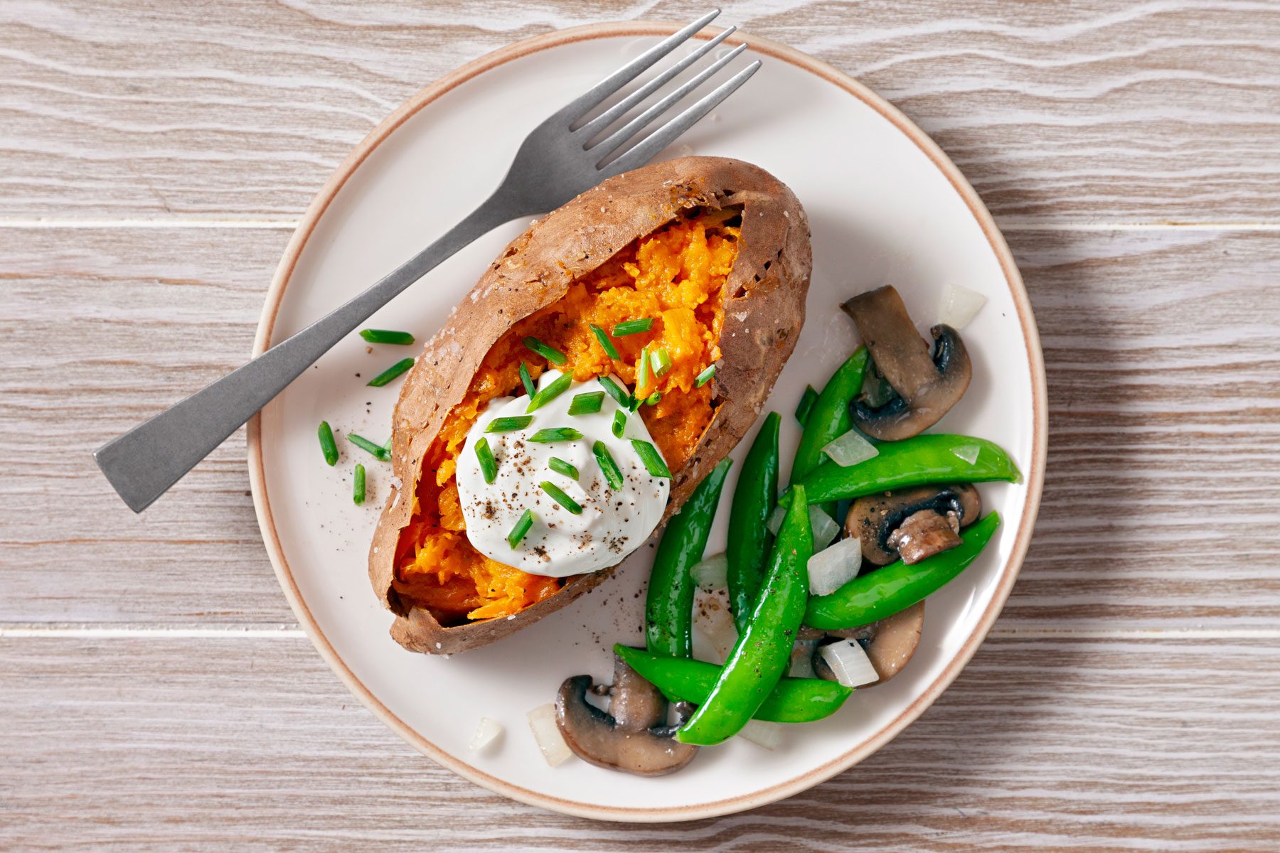 Baked Sweet Potato served with beans and mushrooms on a white plate.