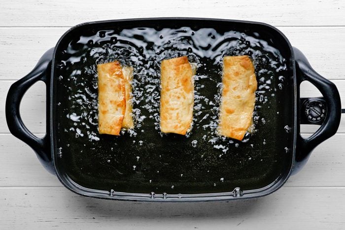 Chimichangas being fried in a skillet.