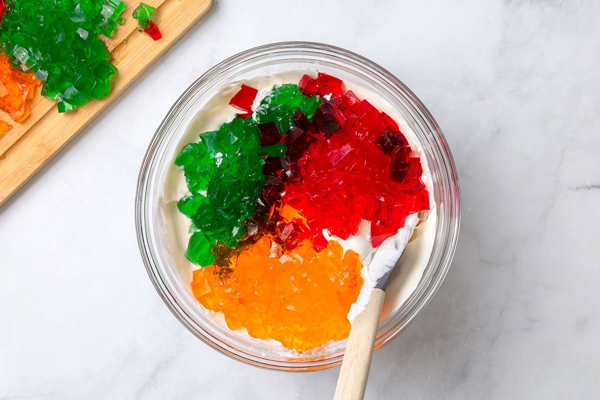 Cubed lime, strawberry and orange jello in a mixing bowl with cool whip and pineapple juice for step three for Broken Glass Jello recipe for Taste of Home
