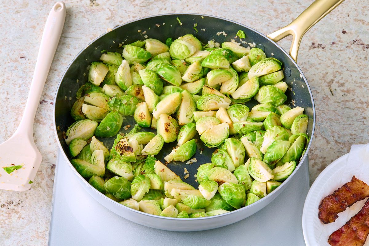 3/4 angle view shot of add Brussels sprouts and shallots to the skillet; cook over medium heat 8-10 minutes or until Brussels sprouts are crisp-tender; spatula; marble surface;