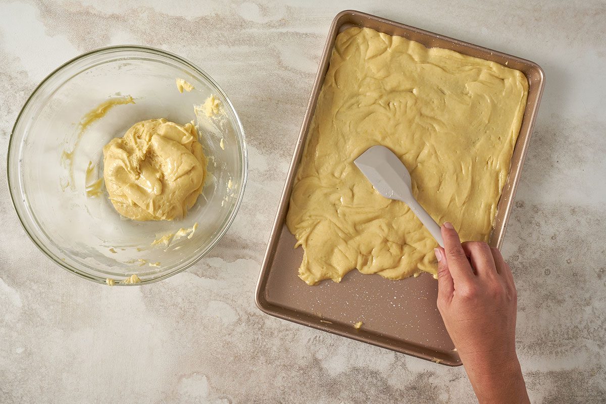 Taste of Home Cake Mix Bars: The first step in preparing the Cake Mix Bars, showing the cake mix combined with eggs and oil, and being spread evenly in a greased baking pan.