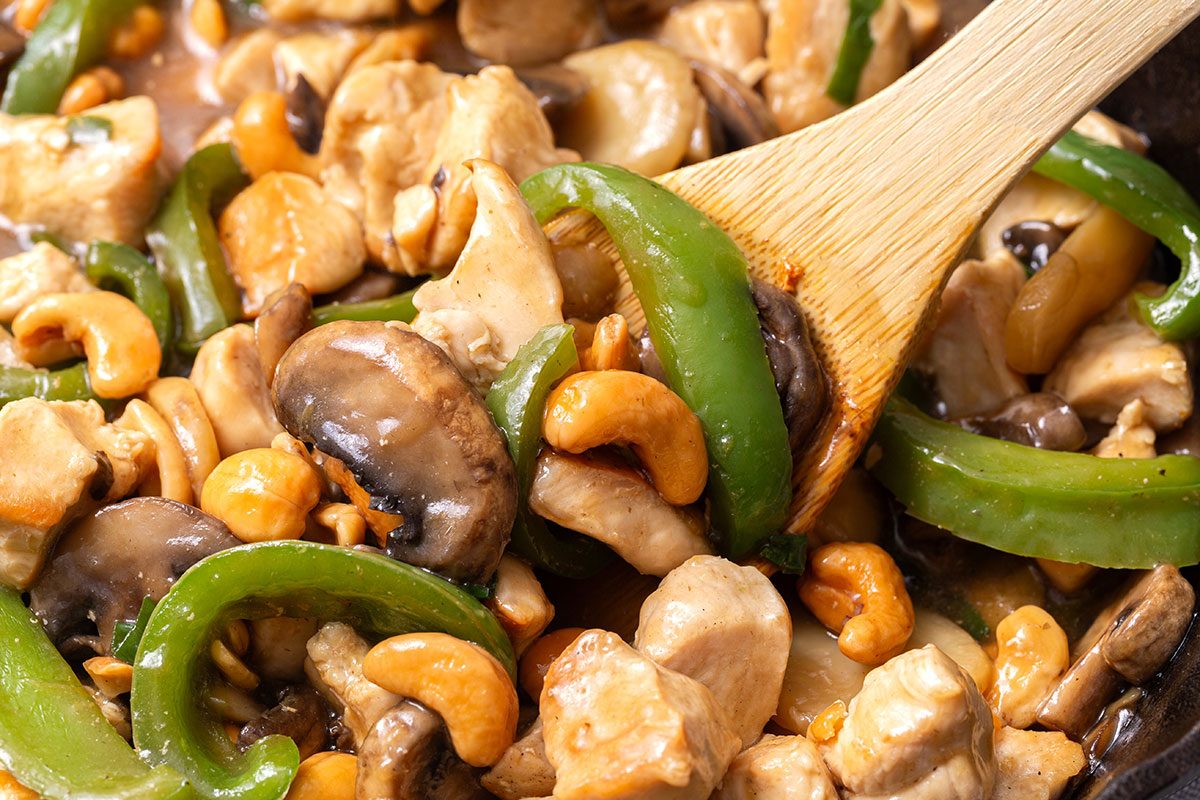 Close up of Cashew Chicken stir fry in a cast iron skillet being served out with a wooden spoon for Taste of Home