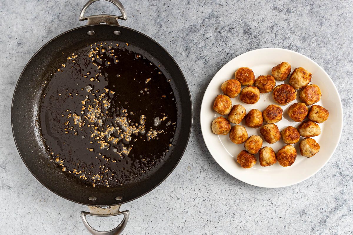 cooked meatballs resting on a plate while garlic is added to the skillet.