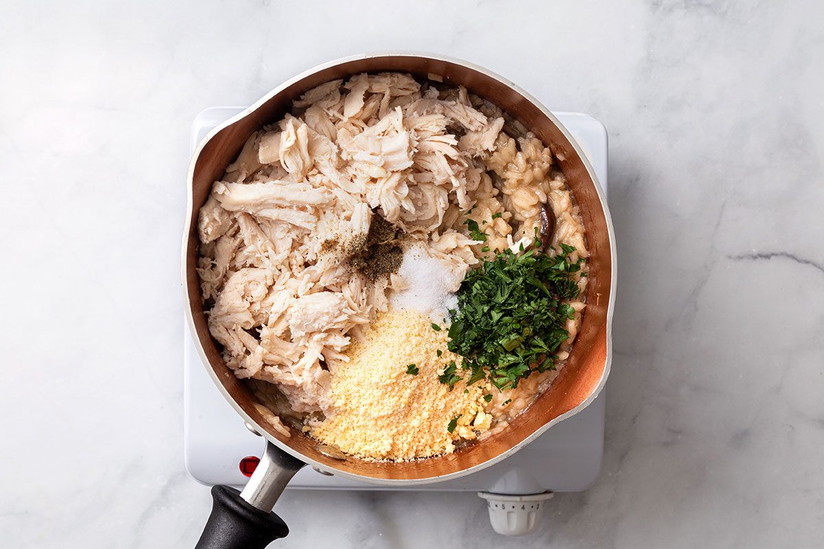 Shredded rotisserie chicken, grated parmesan, minced parsley and salt added to risotto mixture for step five of Chicken Risotto recipe for Taste of Home