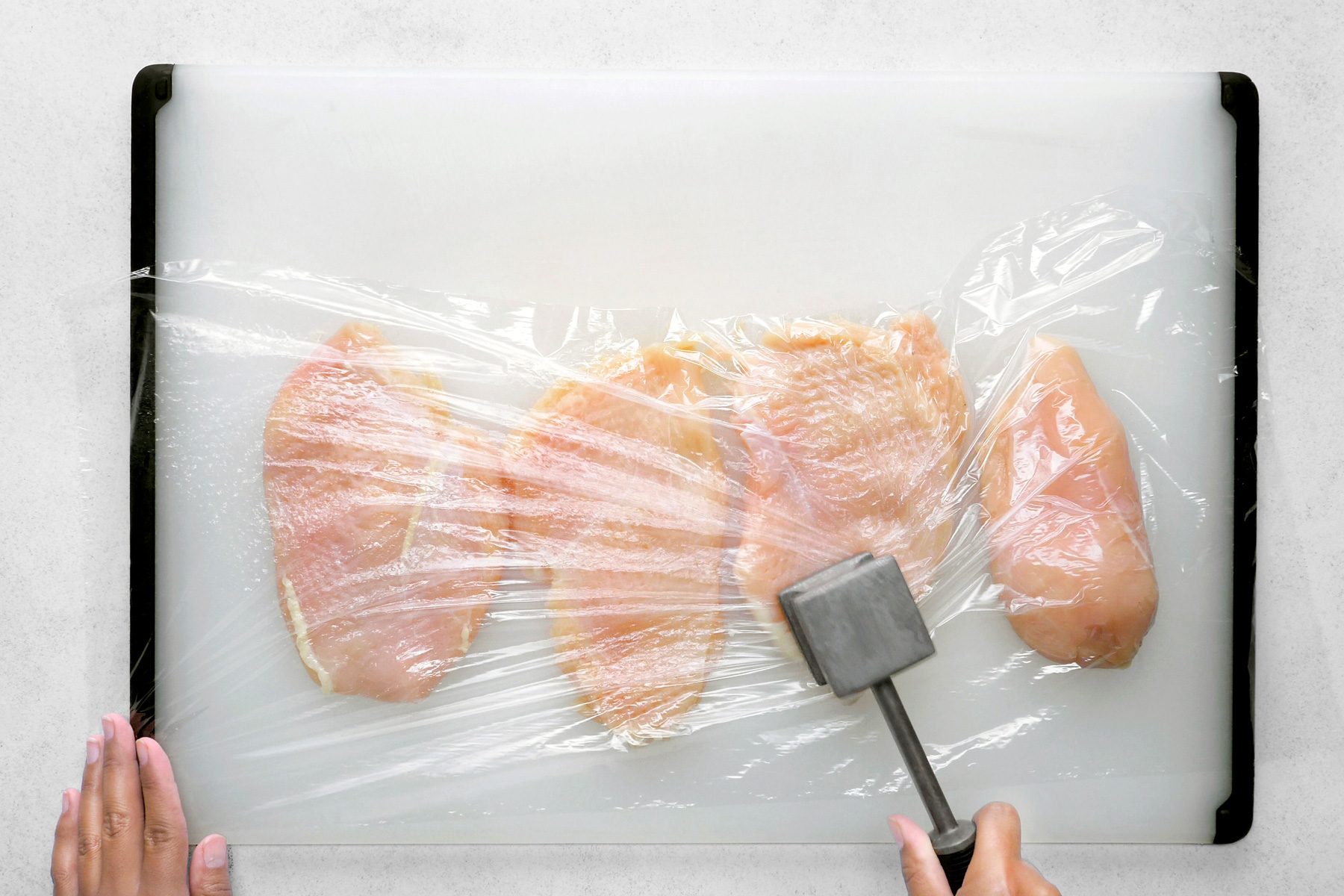 A chicken breast is being pounded with a meat mallet to ensure an even thickness for cooking.