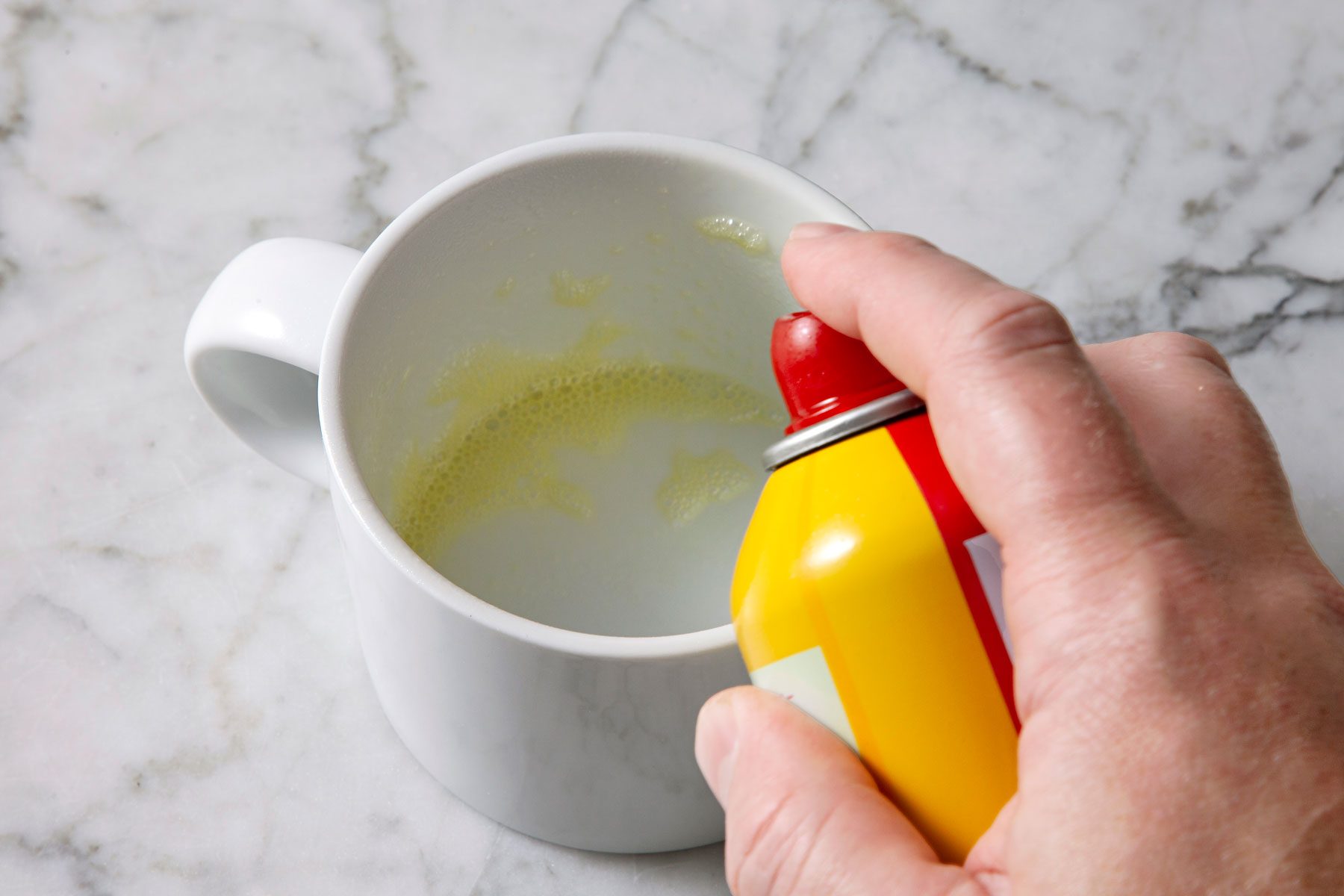 12-ounce microwave-safe coffee mug being sprayed with cooking spray