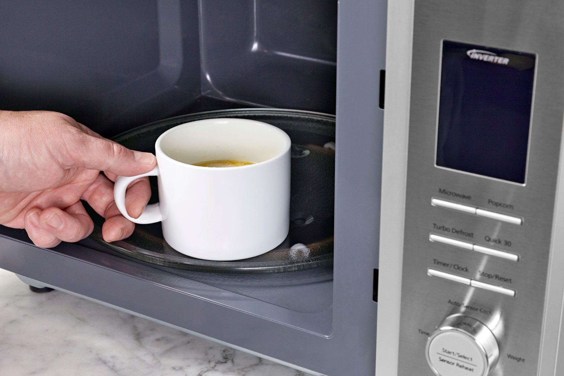 A hand can be seen placing the mug in a microwave.